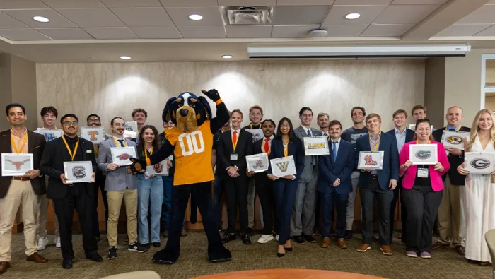 Students participating in the 2024 SEC Pitch competition hold signs featuring their respective university logo and pose with Smokey