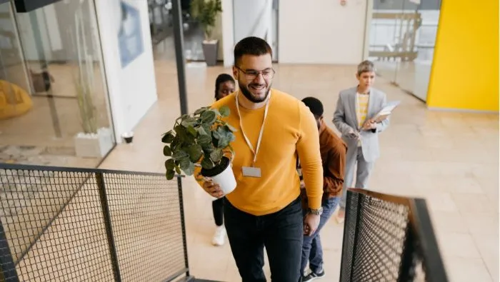 A casually dressed businessman carries a plant into his office building as he returns to work.