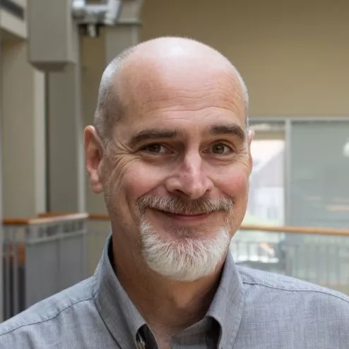 Scott McNutt wearing gray, collared business shirt, standing on the balcony of the Haslam Business Building atrium