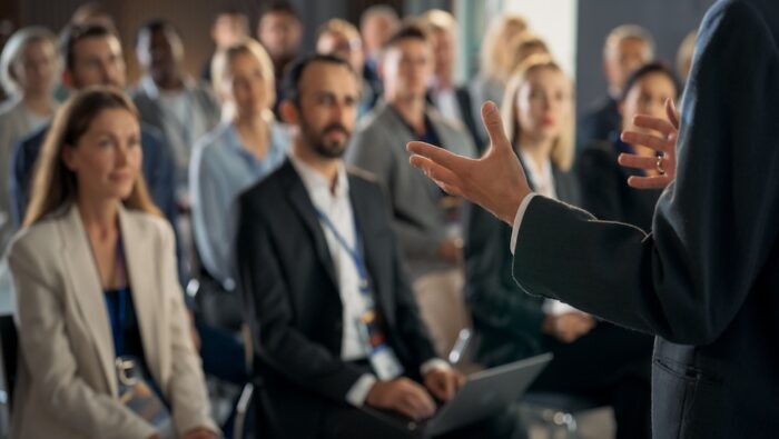 Back view of CEO gesturing And presenting to audience of diverse business leaders