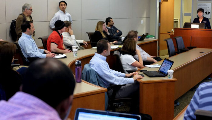 Multi-ethnic group of graduate students in theater-seating style classroom listen to a lecturer.