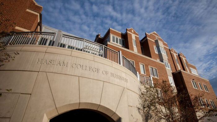 Photo of exterior of Haslam Business Building taken from the ground looking updward with white clouds streaming through the blue sky above it